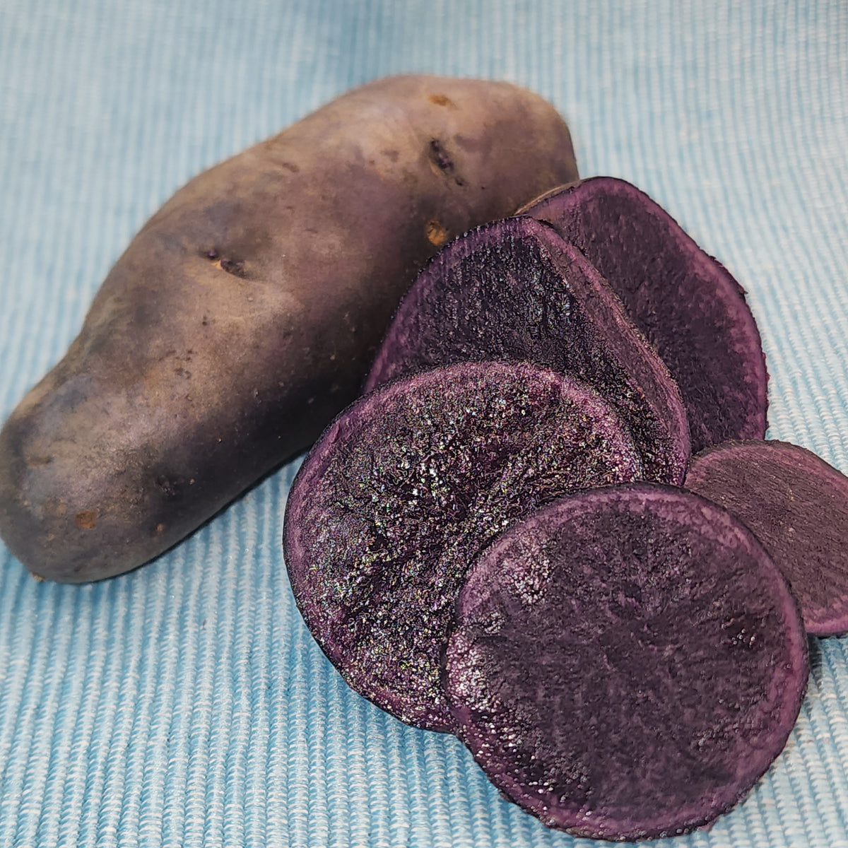 Purple Peruvian Fingerling potato seed from SeedsNow-Potatoes, showing elongated purple-skinned tubers with smooth surface.